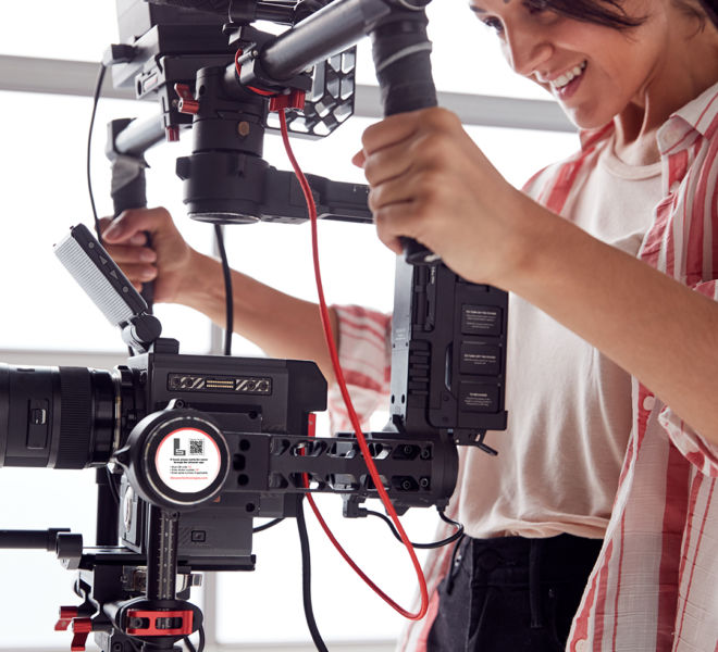 Female Videographer With Video Camera On Steady Cam Rig Filming Movie In White Studio